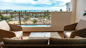 Un balcón con mobiliario de mimbre, vista a una piscina y un paisaje urbano distante.