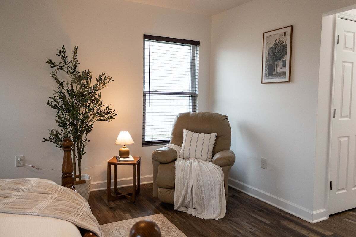 Een slaapkamer met een bed, een stoel, een lamp, een raam en een deur.