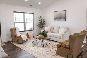 Uma sala de estar com sofá, duas poltronas, mesa de centro, abajur e uma janela grande.