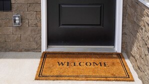 A black door with a decorative glass panel, a doormat with 'WELCOME' text, and a stone wall. - Relaxing Retreat Near Bourbon Trail & Horse Country (Cynthiana)