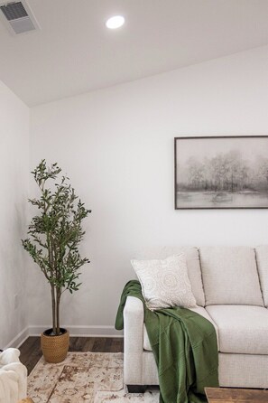 Uma sala de estar com um sofá branco, um cobertor verde, uma planta em vaso e um quadro na parede.
