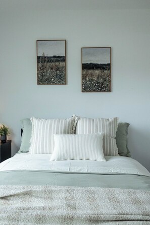 Um quarto com cama, almofadas e duas quadros na parede.