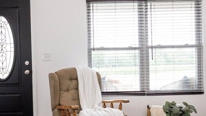 A living room with a large window, a black door with a decorative glass panel, a beige armchair with a white throw, and a coffee table with a woven tray. - Relaxing Retreat Near Bourbon Trail & Horse Country (Cynthiana)