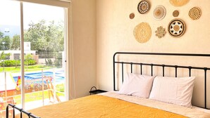 A bedroom with a bed, a view of a swimming pool, and a wall with decorative items.