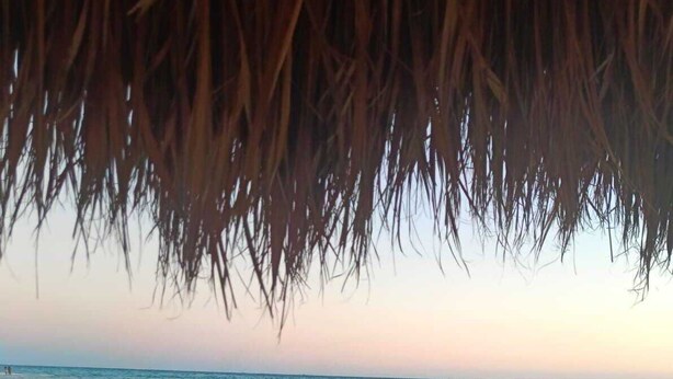 A beach with a thatched roof structure, sandy beach, and calm sea.