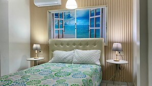 A bedroom with a large bed, two bedside tables with lamps, a window with a view of the sea, and a ceiling fan. - Charming 3-bedroom Apartment Near Puerto Plata's Malecon (Puerto Plata)