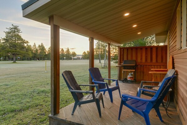 Un espace extérieur abrité comprenant trois fauteuils Adirondack, un barbecue et une vue sur un champ verdoyant.