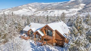 A wooden lodge with a snow-covered roof, large windows, and a deck. - Modern Mountain Stay | Hot Tub, Fire Pit & Views (Silverthorne)