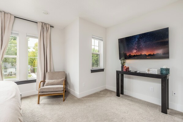 A bedroom with a bed, a chair, a night sky painting, and a nightstand with candles and books.