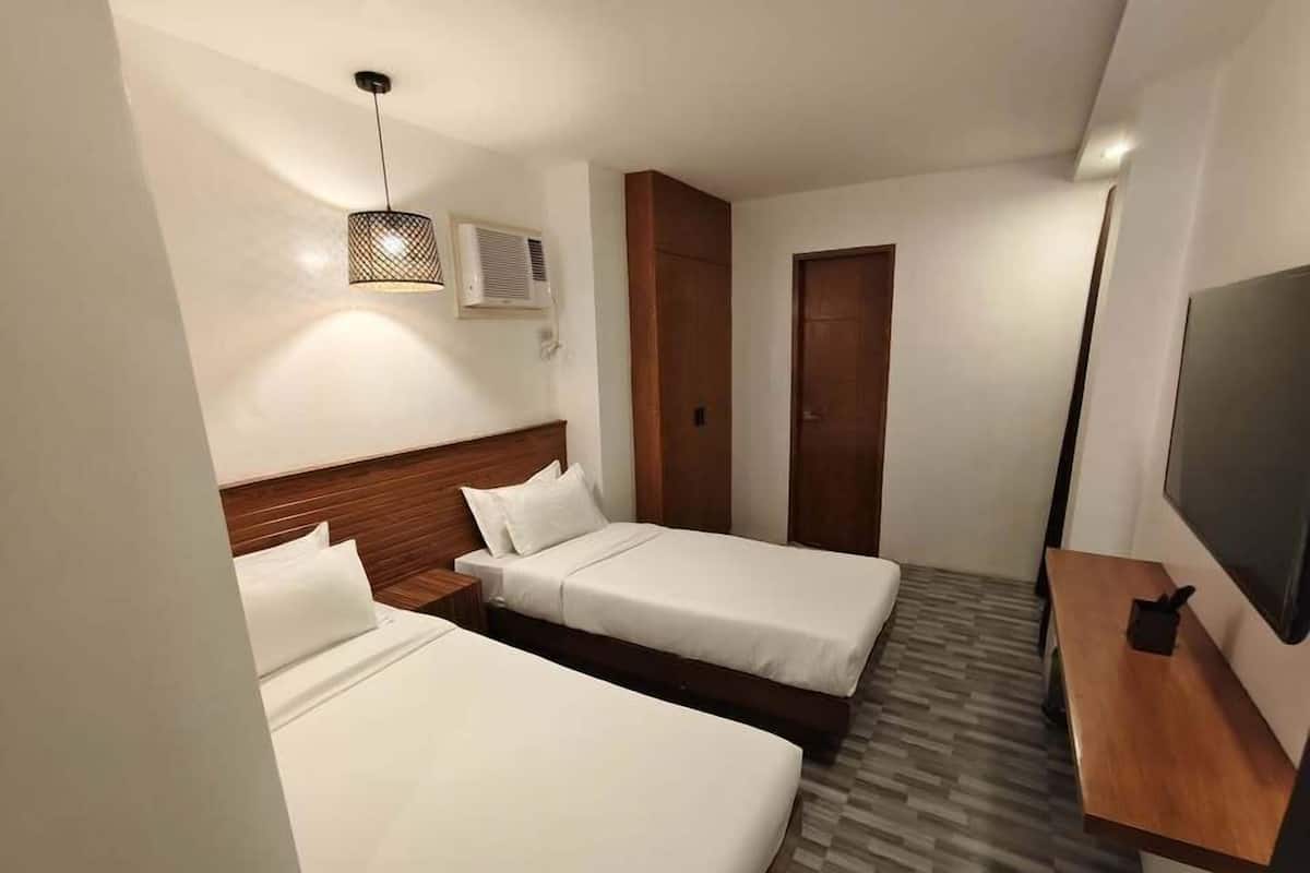 A hotel room with two single beds, a wooden headboard, a TV, a wooden side table, and a patterned floor.