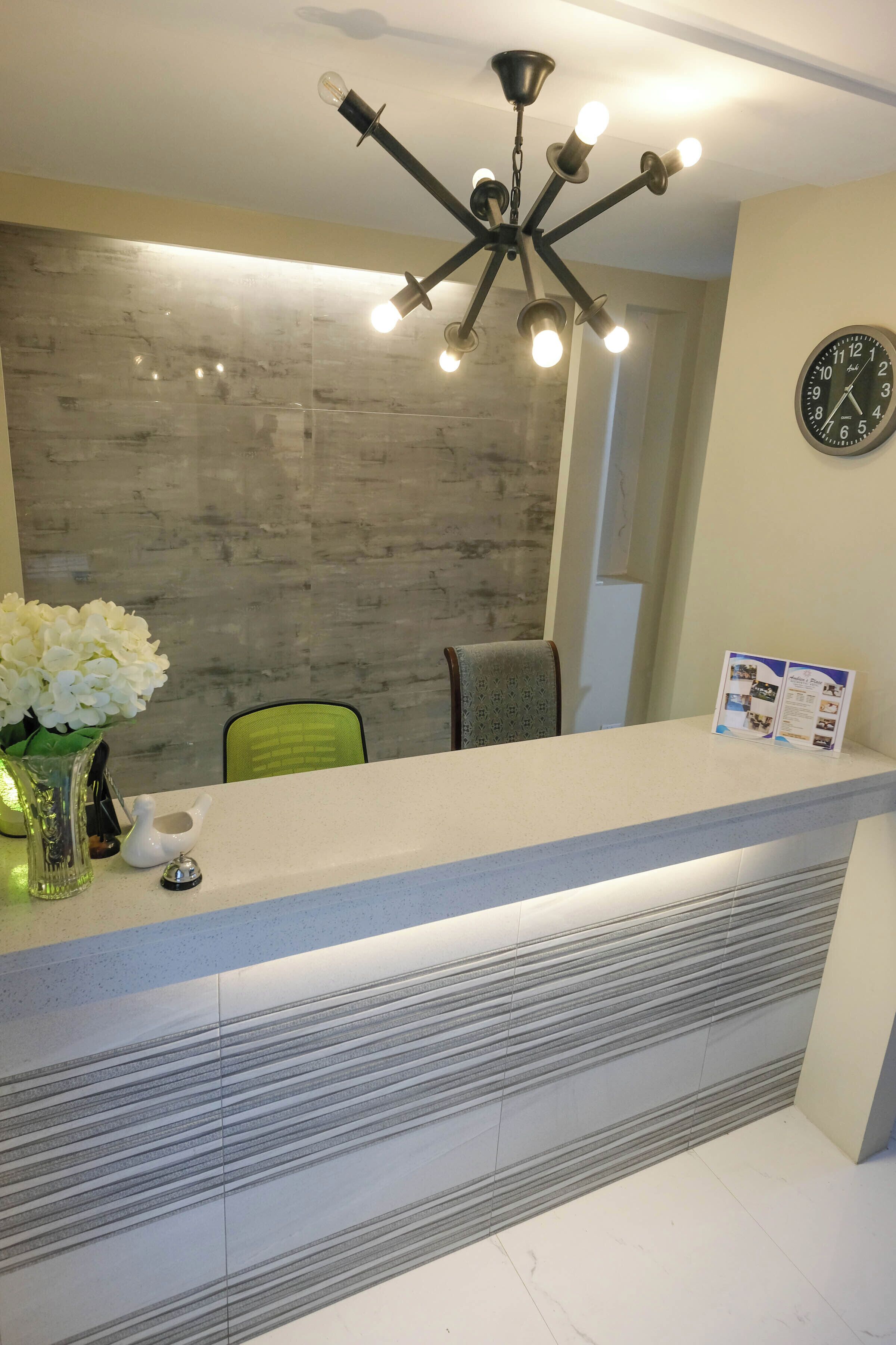 A reception desk with a modern chandelier, a clock, and a vase with white flowers.