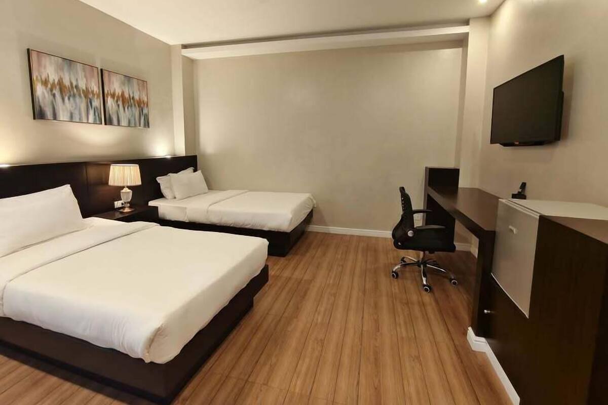 A hotel room with two beds, a desk, a chair, a TV, and abstract art on the wall.
