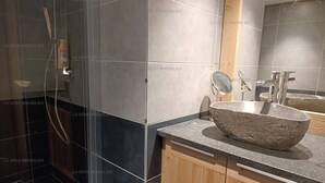 Een moderne badkamer met een stenen wastafel, houten kastjes en een glazen douchecabine.