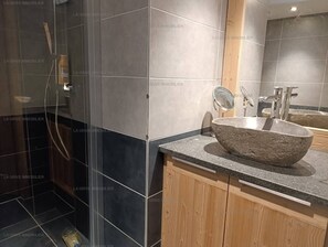 A modern bathroom with a stone sink, wooden cabinets, and a glass shower enclosure.