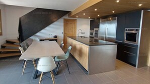 Een moderne keuken met een centraal eiland, inbouwapparatuur en een eethoek met een tafel en stoelen.