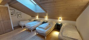 A small, cozy attic bedroom with two beds, a skylight, and a wooden ceiling.