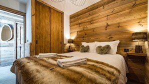 Une chambre à coucher avec une tête de lit en bois, un grand lit recouvert de draps blancs, un plaid en fourrure et deux lampes de chevet.