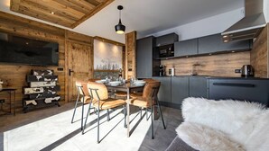 Une cuisine moderne agrémentée d’éléments en bois, un coin repas avec une grande table et des chaises, et un espace salon confortable avec un plaid en fourrure.
