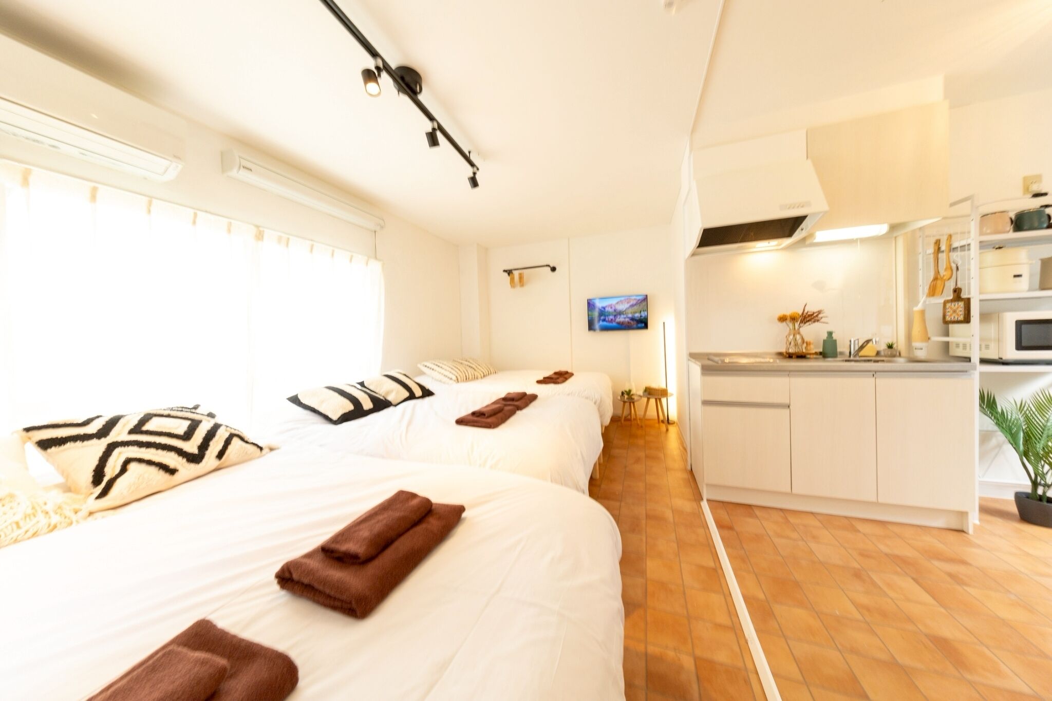 A hotel room with two beds, a kitchenette, and a television.