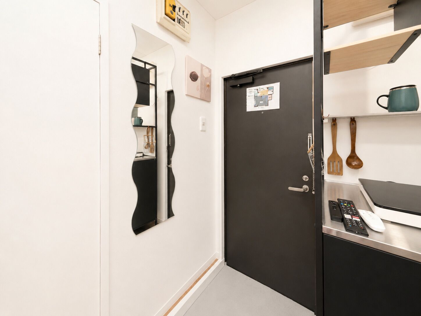A modern kitchen with a black door, a white countertop, and a shelf with kitchen utensils.