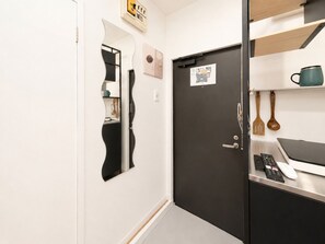 A modern kitchen with a black door, a white countertop, and a shelf with kitchen utensils. - NEST BASE IKEBUKURO (Tokyo)