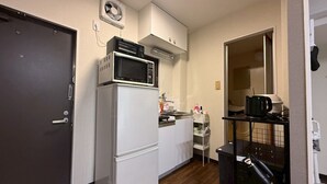 A compact kitchen with a white refrigerator, a microwave on top, a sink, and a small countertop with a kettle and a coffee maker. - NEST BASE IKEBUKURO (Tokyo)