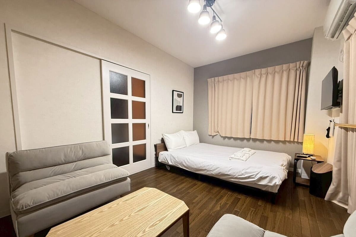 Quarto de hotel com cama, sofá, mesa de madeira e televisão.