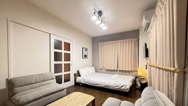 A modern hotel room with a sofa, a bed, a wooden coffee table, and a nightstand. - NEST BASE IKEBUKURO (Tokyo)