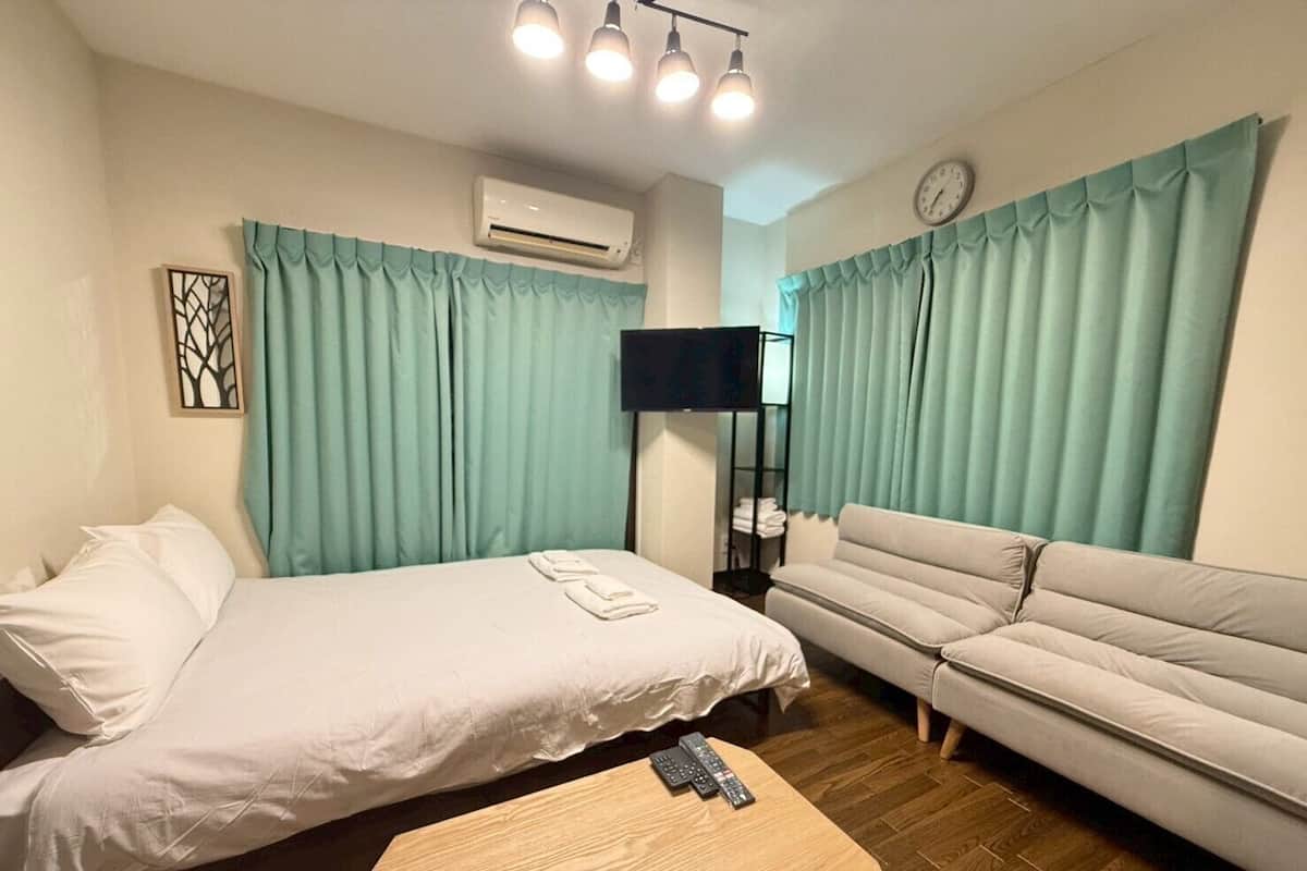 Quarto de hotel com cama, sofá, mesa de madeira e ar condicionado.