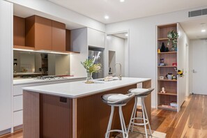 Une cuisine moderne dotée d’un îlot central, de tabourets de bar, d’un four encastré et d’un pare-feu en miroir.