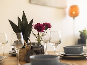 Uma mesa de jantar com uma planta em vaso, um vaso com flores e vários copos e taças de vinho.