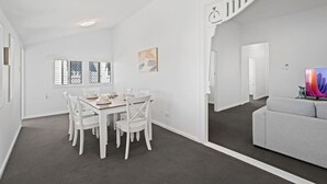 A modern, white-walled room with a dining area, a grey sofa, and a staircase.