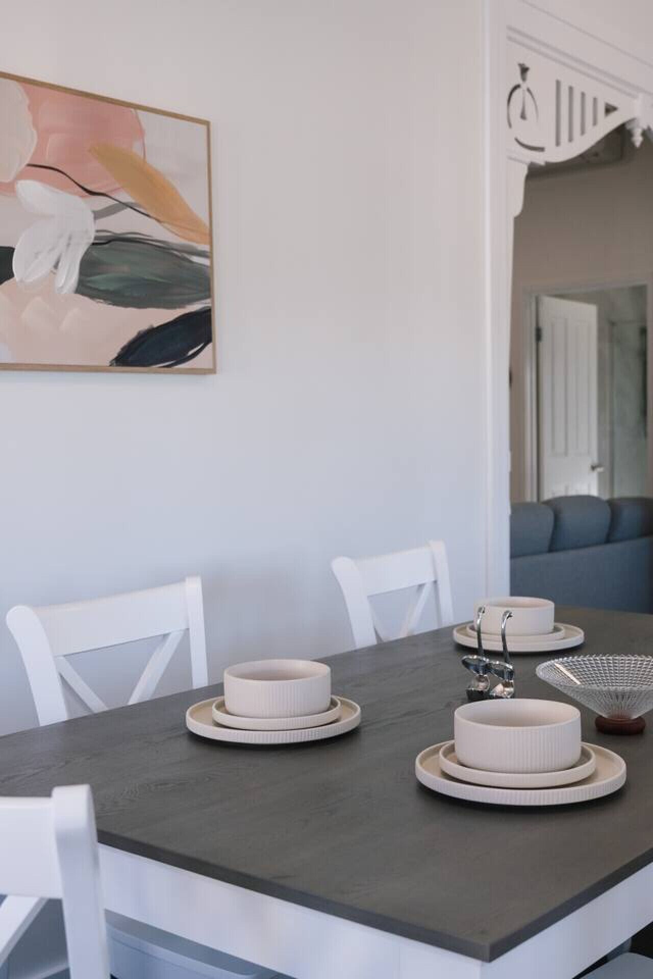 A dining area with a dark wooden table, white chairs, and a modern abstract painting on the wall.