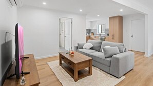 A modern living room with a grey sofa, a wooden coffee table, and a flat-screen TV. - Bright 3BR Home| 2 Baths |Close to CBD & Hospitals (Herston)