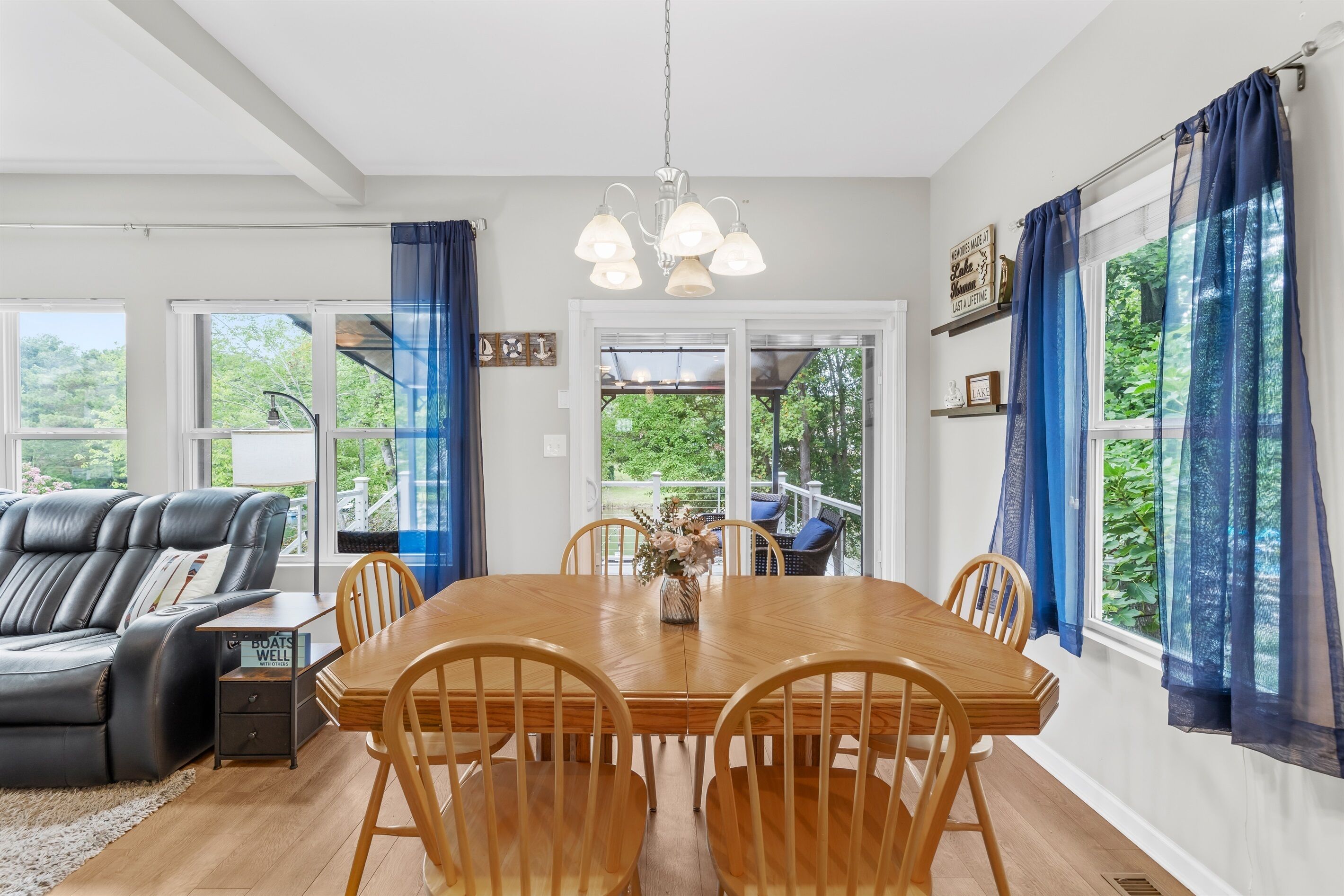Un comedor con una mesa y sillas de madera, una araña y ventanas grandes con cortinas azules.
