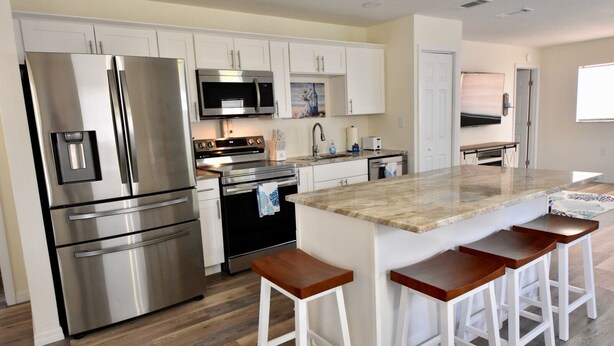 A modern kitchen with stainless steel appliances, white cabinetry, and a central island with bar stools.