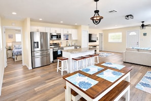 A modern kitchen with stainless steel appliances, a central island with bar stools, and a dining area with a wooden table.