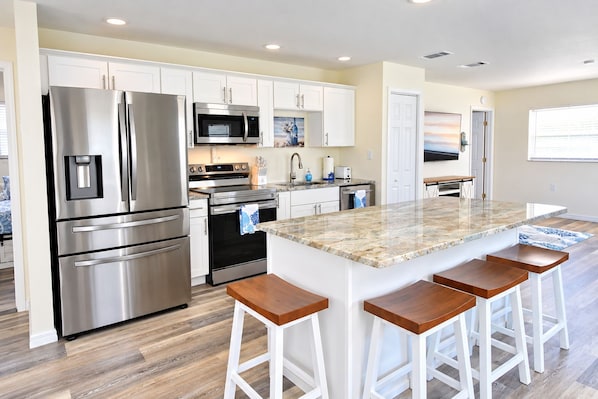 A modern kitchen with stainless steel appliances, white cabinetry, and a central island with bar stools.