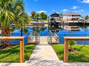 A marina with a dock leading to a house, surrounded by water and greenery.