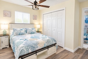 A bedroom with a bed, nightstands, a ceiling fan, a window with blinds, a white closet, and a bathroom visible through an open door.