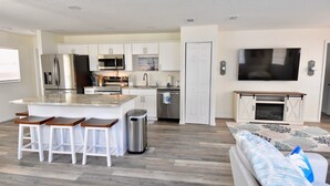 A modern kitchen with white cabinets, a central island with stools, a stainless steel refrigerator, and a microwave.