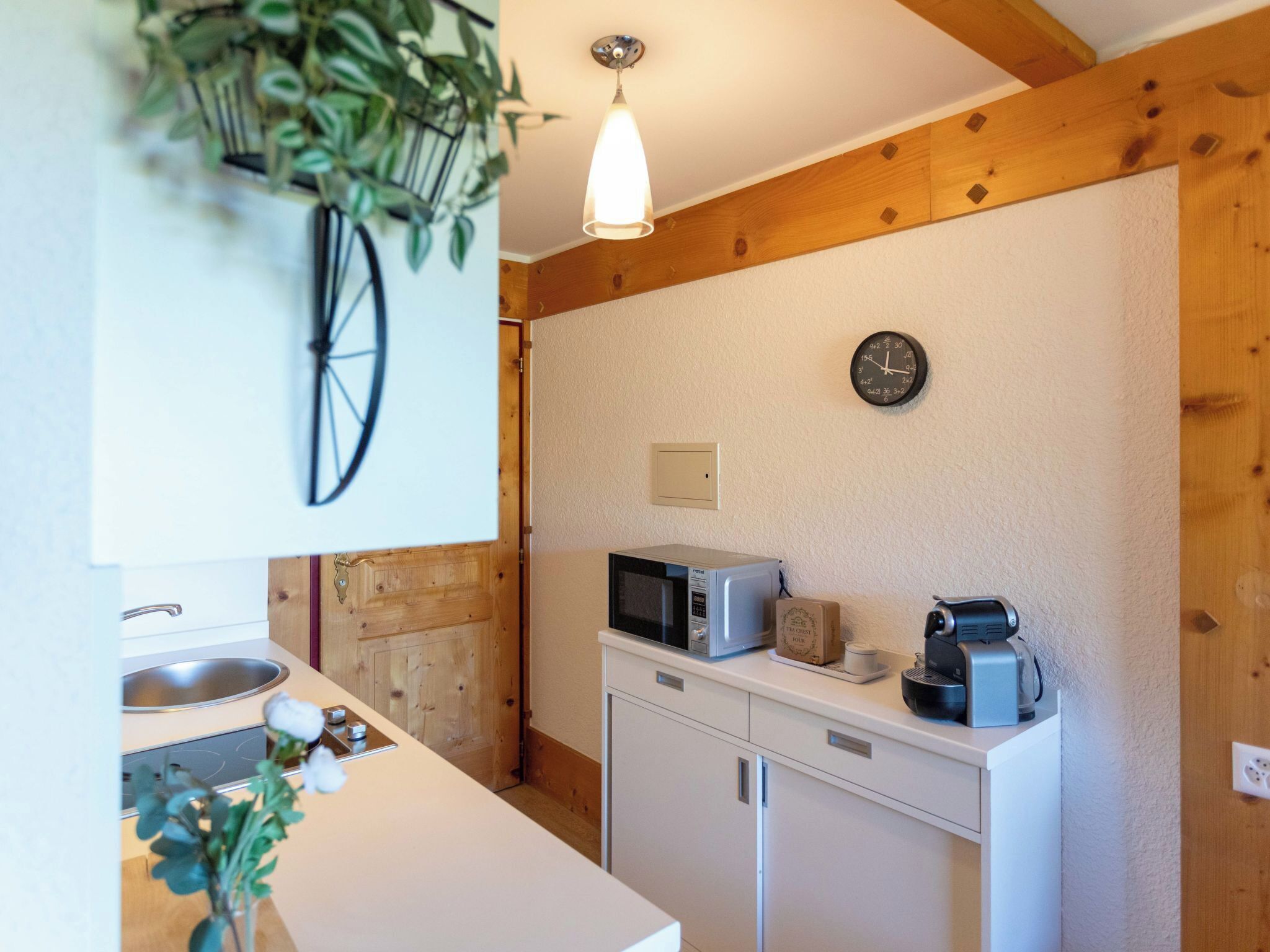 Une cuisine de taille réduite avec des poutres en bois, une horloge, un four à micro-ondes et une machine à café.