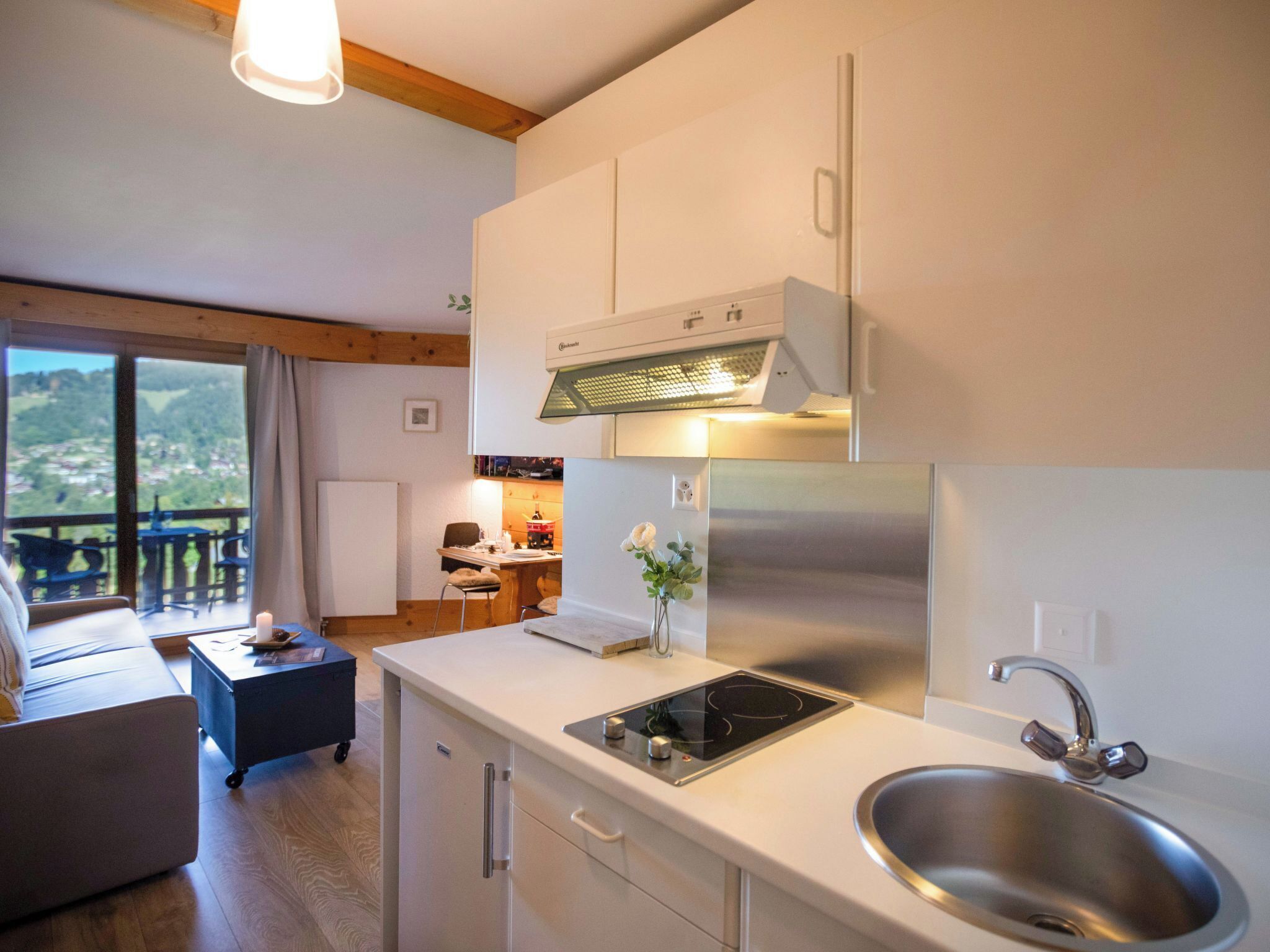 A modern kitchen with a stainless steel refrigerator, a built-in oven, and a sink. There is a dining area with a table and chairs visible through a large window.
