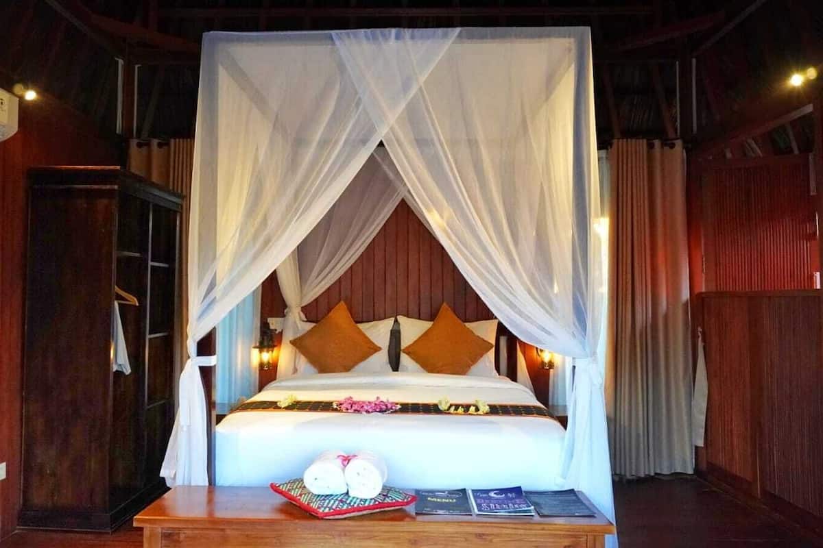 A bed with a canopy, wooden walls, a bedside table with a menu, and a wall-mounted air conditioner.