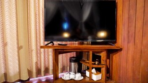 Een televisie op een houten standaard, met een afstandsbediening, een koffiezetapparaat en een zakdoos.