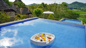 Een zwembad met een hottub in het midden, omgeven door weelderige begroeiing en uitzicht op een berg.