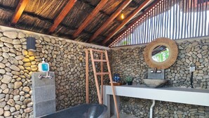 A stone-walled bathroom with a freestanding bathtub, a wooden ladder, a sink, and a mirror. - Golo Pada Villa Labuan Bajo by ABM (Labuan Bajo)