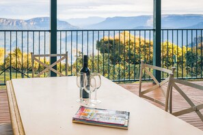 Une table avec un magazine, une bouteille et trois verres, sur un balcon donnant sur les montagnes.