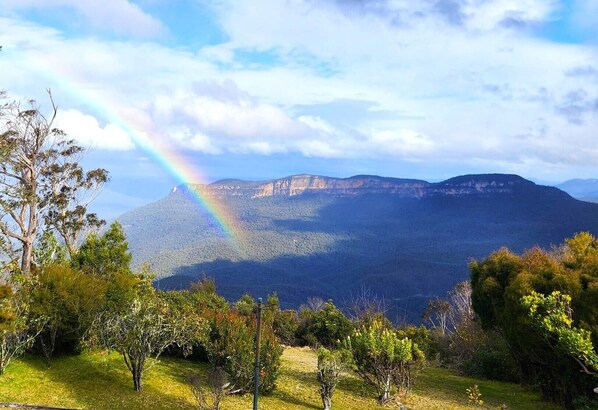 Un paysage de montagne avec un arc-en-ciel, des arbres et un premier plan herbeux.