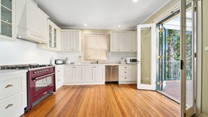 A modern kitchen with white cabinetry, a red stove, and a wooden floor. - Blue Mountains Rhapsody - Point Blank Views Clifftop (Leura)